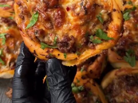Golden puffed poğaça on a baking sheet, with one side torn open revealing juicy ground beef and stretchy melted cheese.