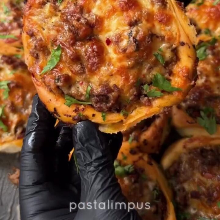 Golden puffed poğaça on a baking sheet, with one side torn open revealing juicy ground beef and stretchy melted cheese.