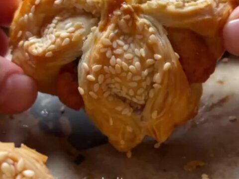 Golden sesame-crusted pastry pockets on a baking sheet, one broken open to show fluffy herbed potato filling