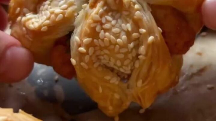 Golden sesame-crusted pastry pockets on a baking sheet, one broken open to show fluffy herbed potato filling