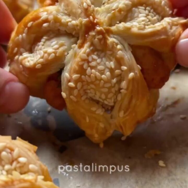 Golden sesame-crusted pastry pockets on a baking sheet, one broken open to show fluffy herbed potato filling