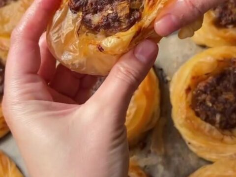 Golden, flaky kaytaz böreği pastries on a serving plate, with one broken open to show the juicy meat filling.