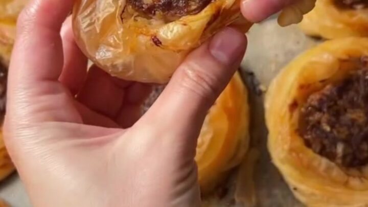 Golden, flaky kaytaz böreği pastries on a serving plate, with one broken open to show the juicy meat filling.