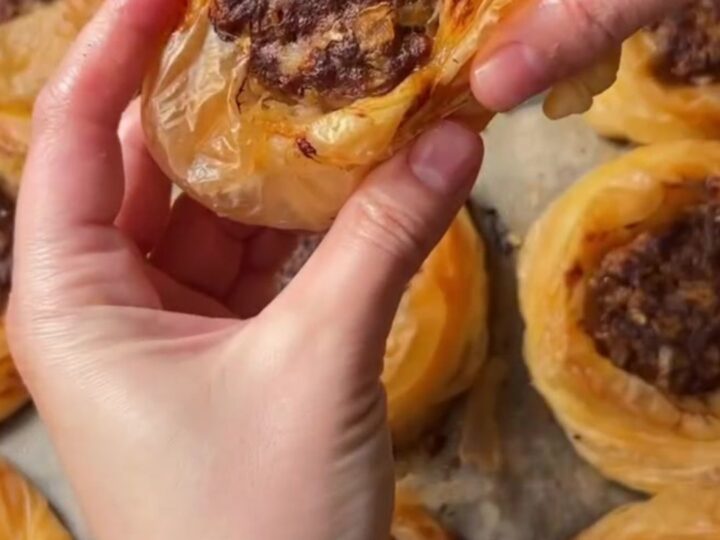 Golden, flaky kaytaz böreği pastries on a serving plate, with one broken open to show the juicy meat filling.