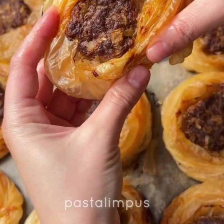 Golden, flaky kaytaz böreği pastries on a serving plate, with one broken open to show the juicy meat filling.