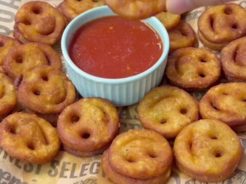 Golden crispy smiley face potato fries on a plate with a small bowl of ketchup