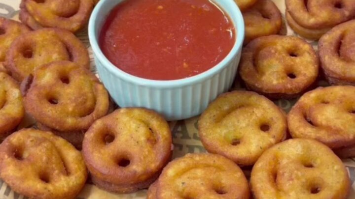 Golden crispy smiley face potato fries on a plate with a small bowl of ketchup