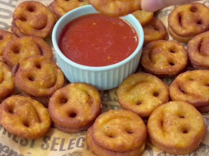 Golden crispy smiley face potato fries on a plate with a small bowl of ketchup