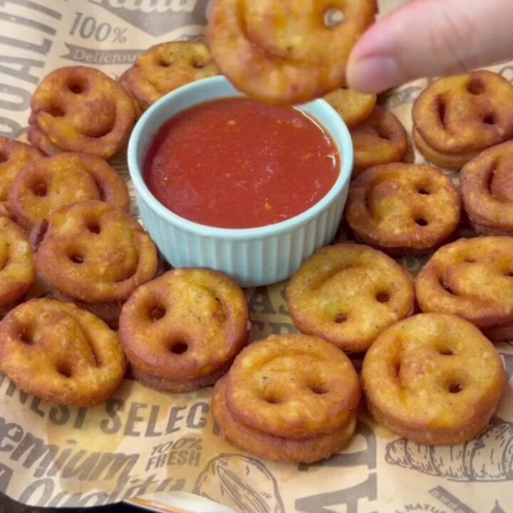 Golden crispy smiley face potato fries on a plate with a small bowl of ketchup