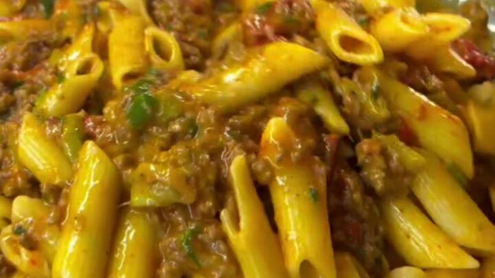 Spoon lifting penne with melted mozzarella and meatball in a bowl