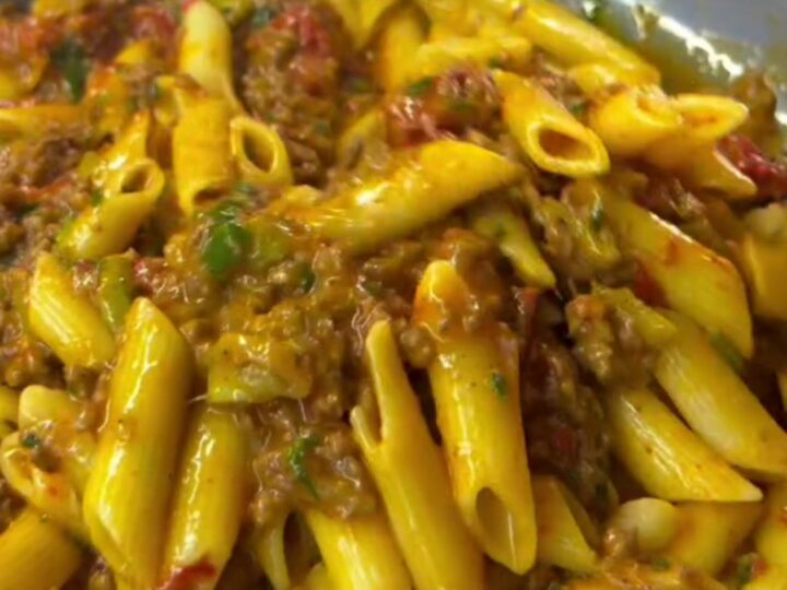 Spoon lifting penne with melted mozzarella and meatball in a bowl