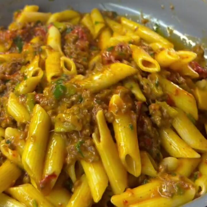 Spoon lifting penne with melted mozzarella and meatball in a bowl