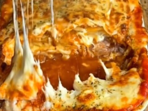 A steaming, golden-brown baked lasagna in a white dish, featuring thick, stretchy cheese pulls.