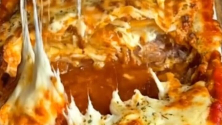 A steaming, golden-brown baked lasagna in a white dish, featuring thick, stretchy cheese pulls.
