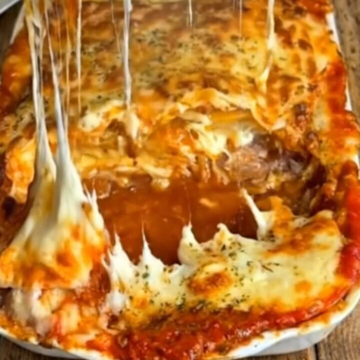 A steaming, golden-brown baked lasagna in a white dish, featuring thick, stretchy cheese pulls.