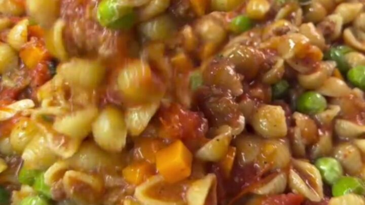 A deep ladle transferring steaming shell pasta with blistered tomatoes into a ceramic bowl, drizzled with olive oil.