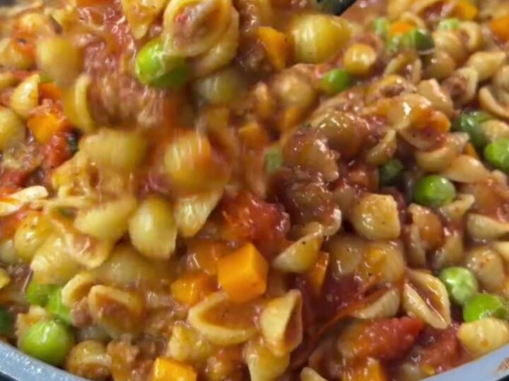 A deep ladle transferring steaming shell pasta with blistered tomatoes into a ceramic bowl, drizzled with olive oil.