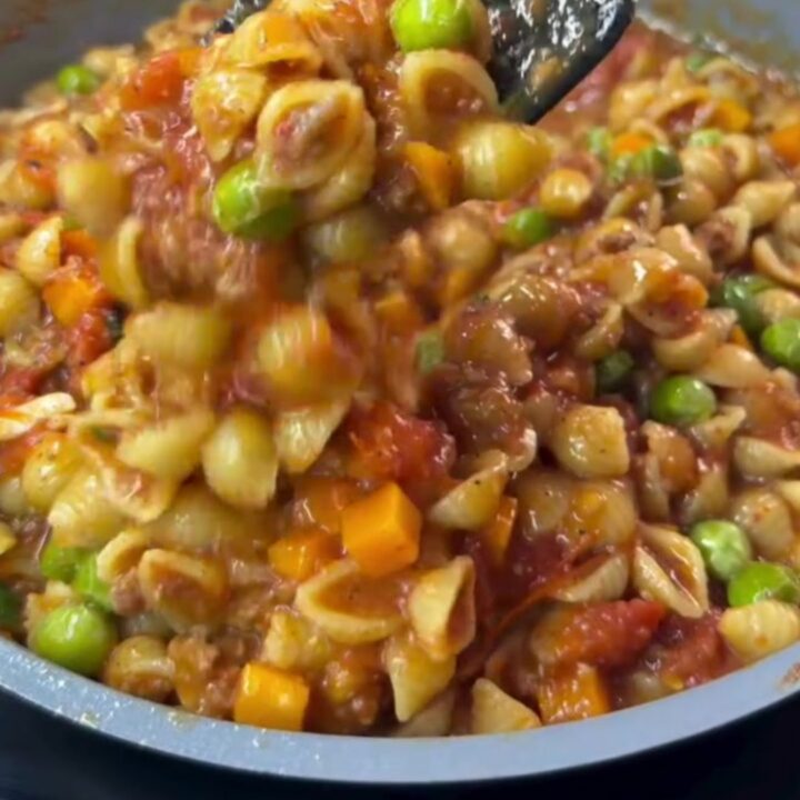 A deep ladle transferring steaming shell pasta with blistered tomatoes into a ceramic bowl, drizzled with olive oil.