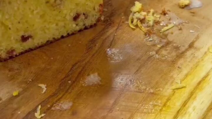 Whole lemon loaf cake with glossy powdered sugar icing, sliced, showing moist crumb