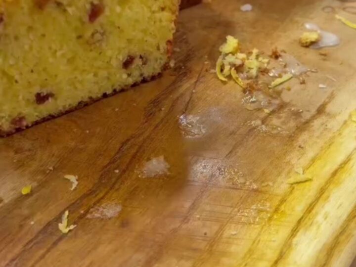 Whole lemon loaf cake with glossy powdered sugar icing, sliced, showing moist crumb