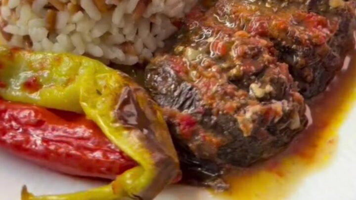 Baked accordion eggplant kebab in a baking dish with tomato sauce, garnished with fresh herbs.