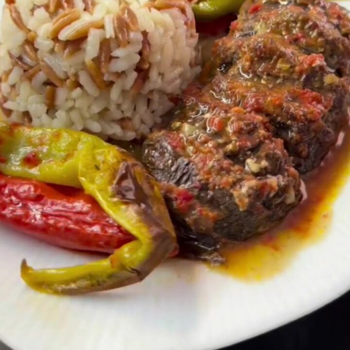 Baked accordion eggplant kebab in a baking dish with tomato sauce, garnished with fresh herbs.