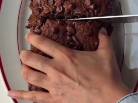 A thick slice of brown butter banana bread with molten chocolate pockets, on a wooden board