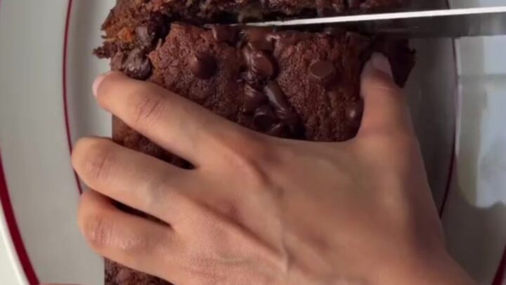 A thick slice of brown butter banana bread with molten chocolate pockets, on a wooden board