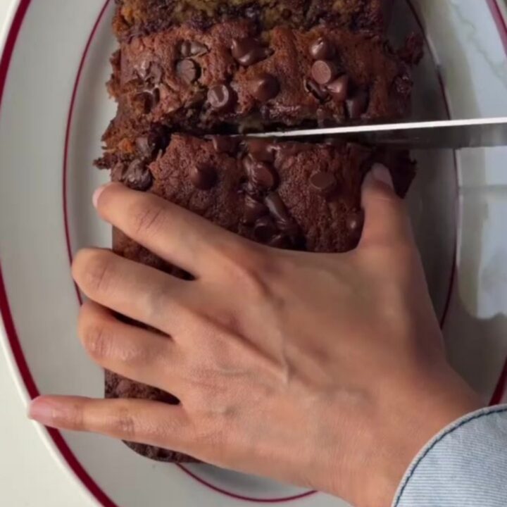A thick slice of brown butter banana bread with molten chocolate pockets, on a wooden board
