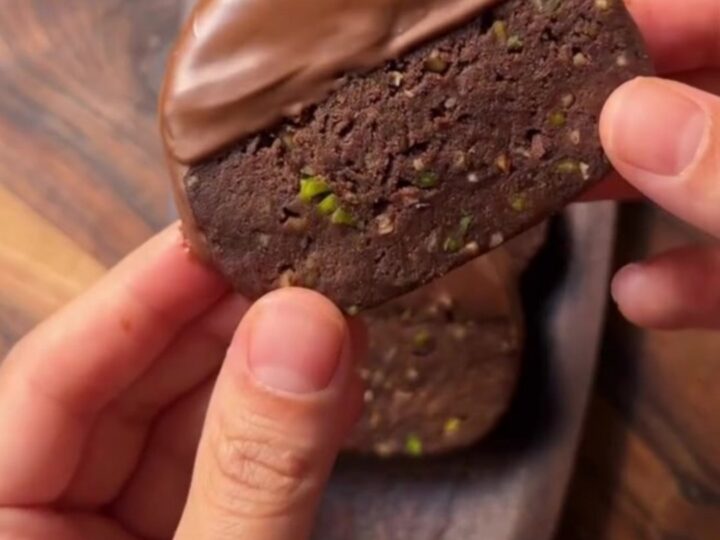 Chocolate-dipped banana biscuit discs with pistachios on parchment paper