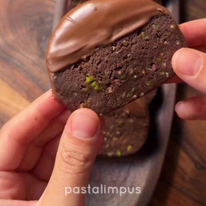 Chocolate-dipped banana biscuit discs with pistachios on parchment paper