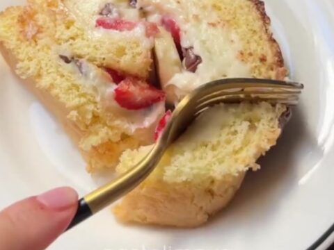 Sliced Swiss roll with white chocolate cream, strawberries, and bananas, dusted with powdered sugar