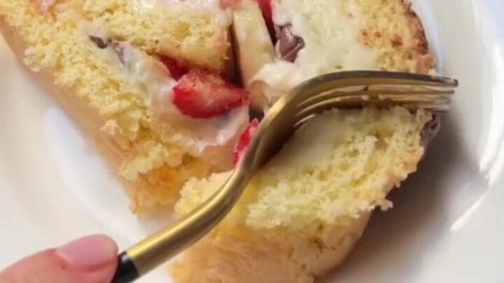 Sliced Swiss roll with white chocolate cream, strawberries, and bananas, dusted with powdered sugar