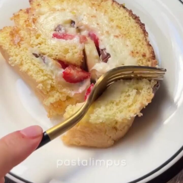Sliced Swiss roll with white chocolate cream, strawberries, and bananas, dusted with powdered sugar
