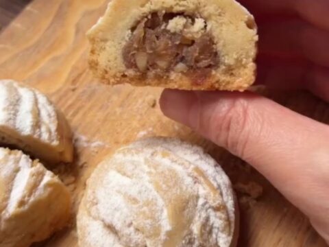 Warm cookies dusted with powdered sugar, one broken open to show apple filling