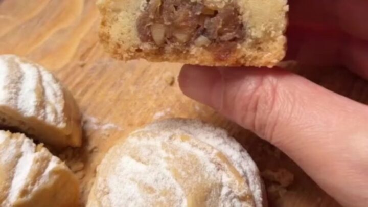 Warm cookies dusted with powdered sugar, one broken open to show apple filling