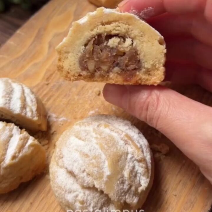 Warm cookies dusted with powdered sugar, one broken open to show apple filling