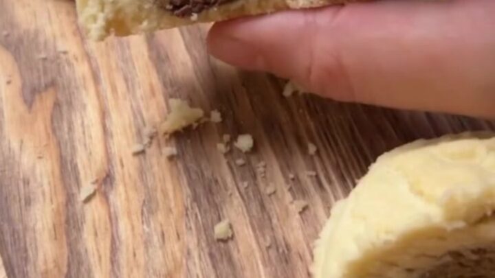 A shortbread cookie broken in half, showing a glossy molten hazelnut chocolate center oozing out