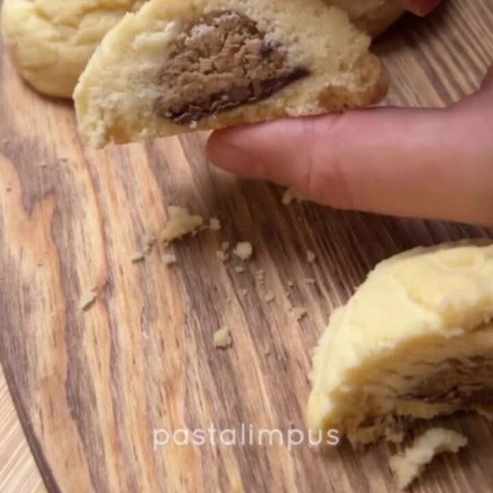 A shortbread cookie broken in half, showing a glossy molten hazelnut chocolate center oozing out