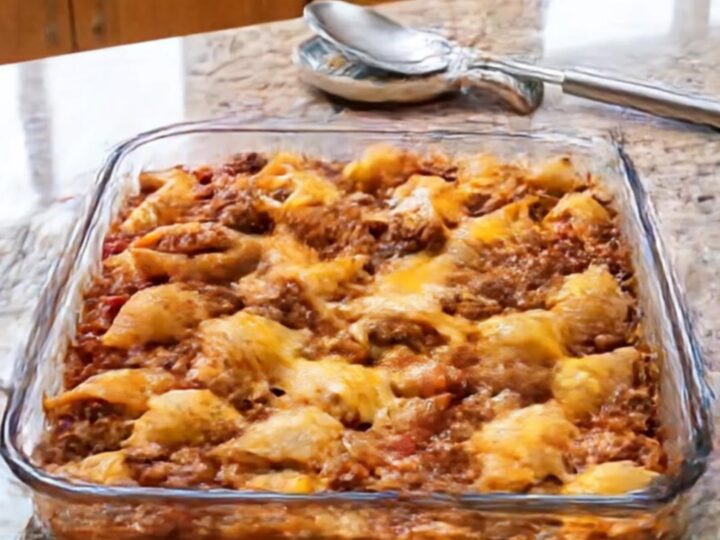 A clear glass baking dish filled with golden, bubbling cheesy beef pasta shells on a granite countertop.