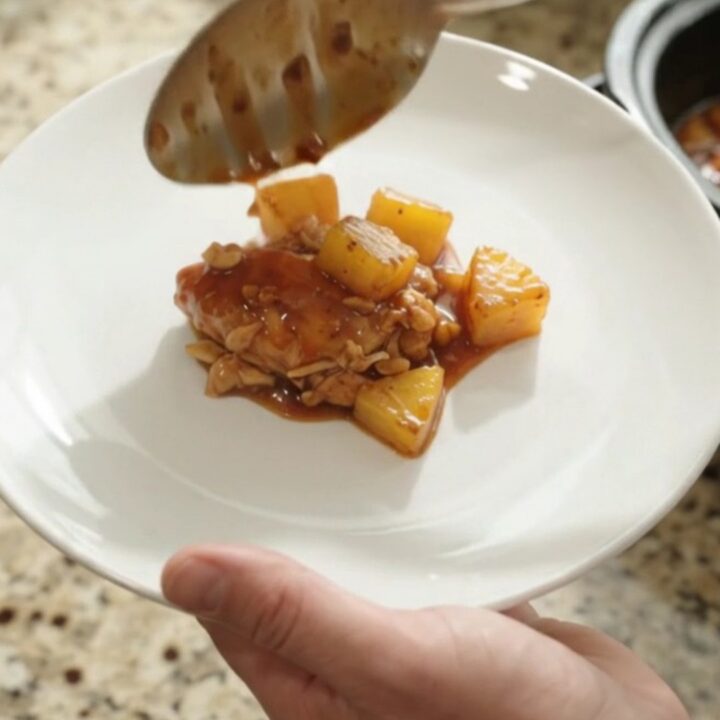Shredded pineapple BBQ chicken in a slow cooker with glossy sauce and caramelized pineapple chunks