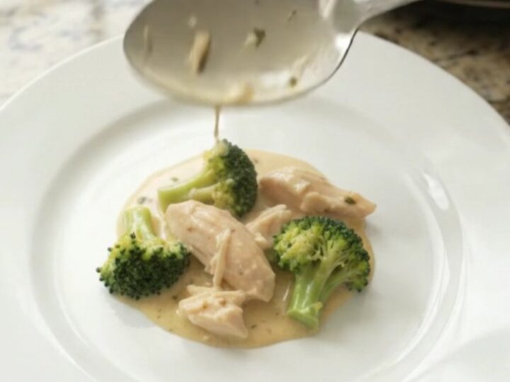 Creamy Crockpot chicken and broccoli with melted cheddar sauce, served in a white bowl
