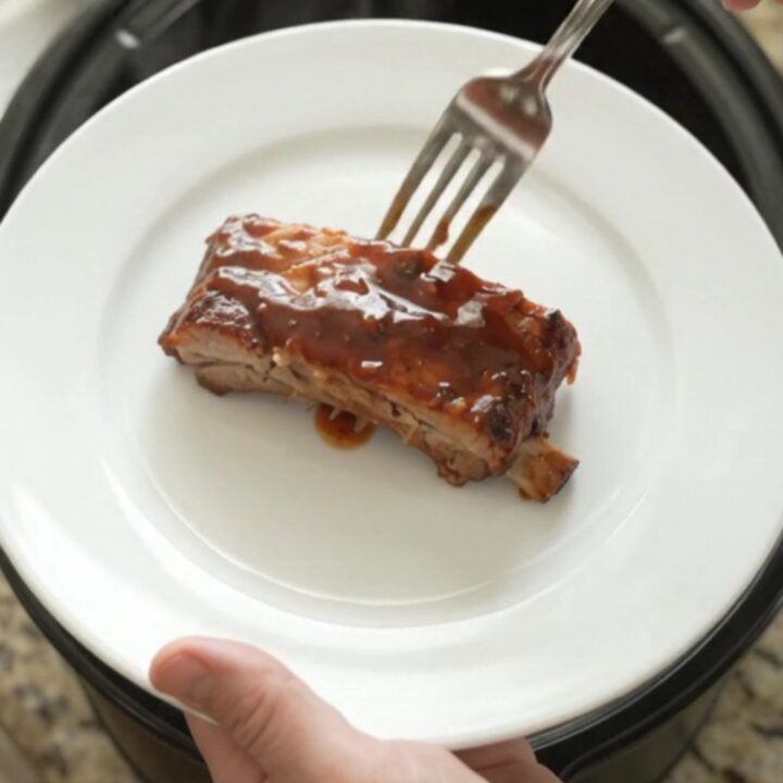 Slow-cooker BBQ ribs glistening with sticky sauce on a white plate.