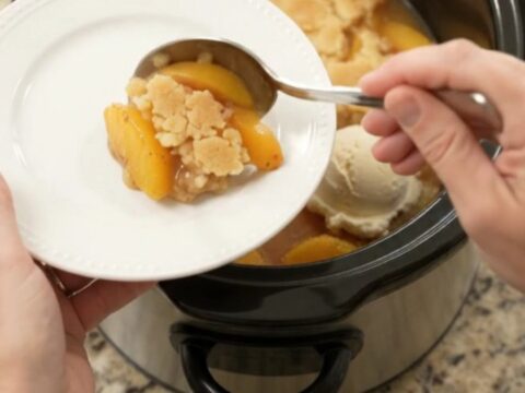 Warm peach cobbler in a black slow cooker with golden crust and bubbling syrup