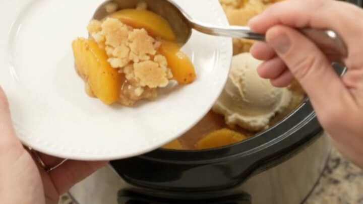 Warm peach cobbler in a black slow cooker with golden crust and bubbling syrup