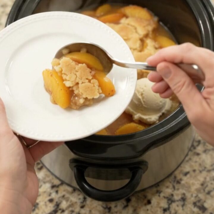 Warm peach cobbler in a black slow cooker with golden crust and bubbling syrup