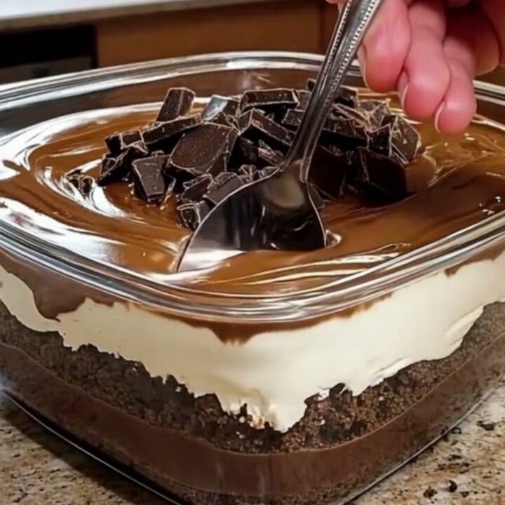 A clear glass dish filled with layers of brownie, whipped cream, and glossy chocolate ganache.