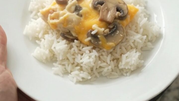 Slow cooker creamy cheddar mushroom chicken in a black crockpot, topped with melted cheese and mushrooms