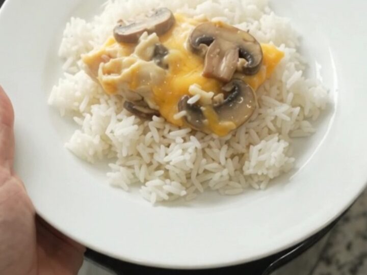 Slow cooker creamy cheddar mushroom chicken in a black crockpot, topped with melted cheese and mushrooms