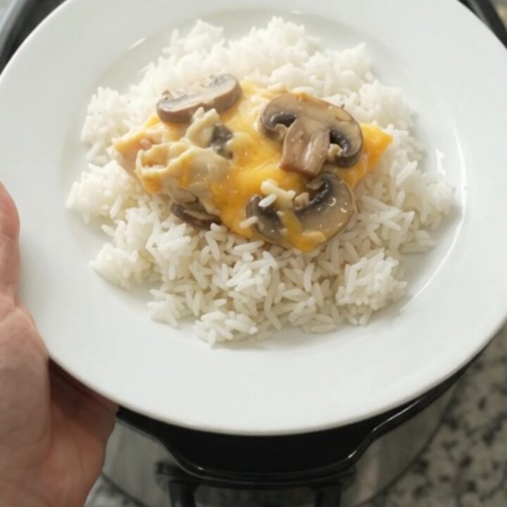 Slow cooker creamy cheddar mushroom chicken in a black crockpot, topped with melted cheese and mushrooms